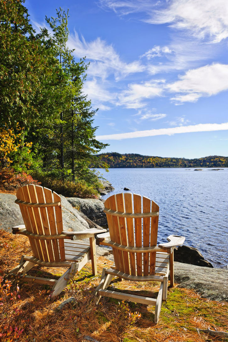 A pair of adirondack chairs on the shore of Lake of Two Rivers in Ontario.