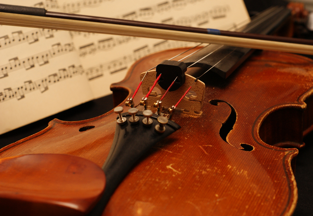 Close up of the body of a violin with sheet music visible in the background.