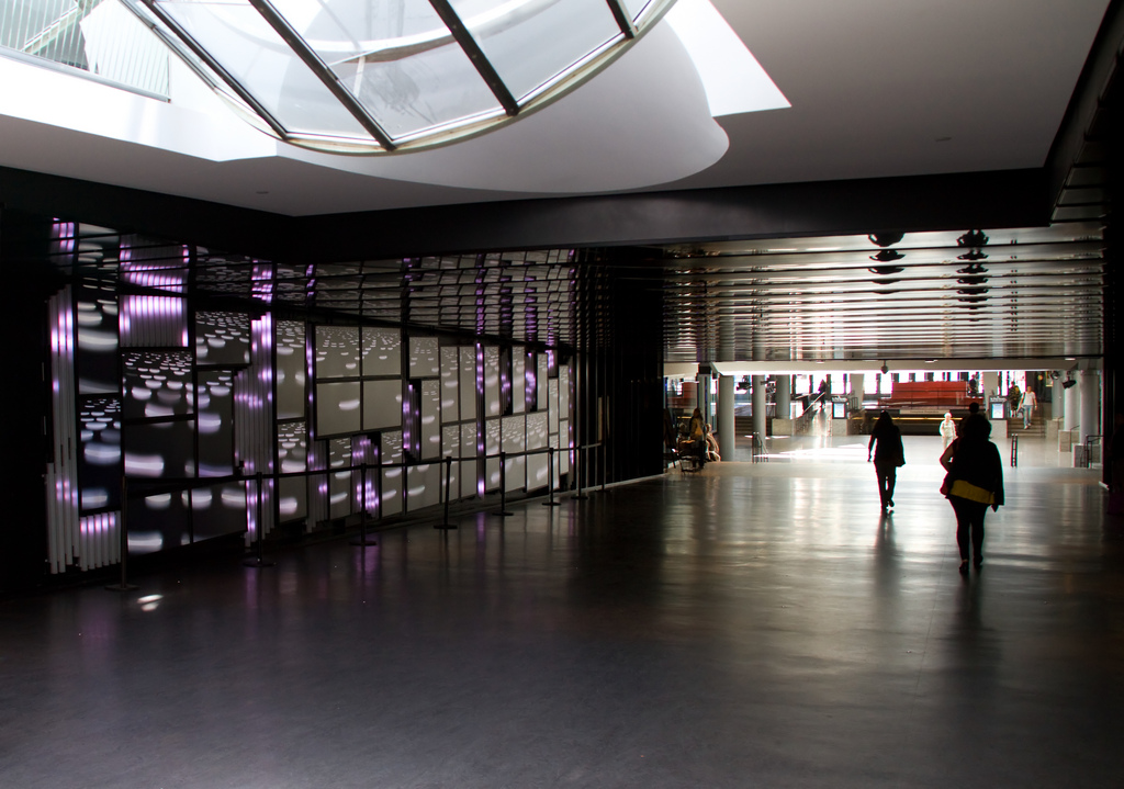 Pedestrians in the underground are silhouetted as light filters through a skylight and reflects on the glossy floors.