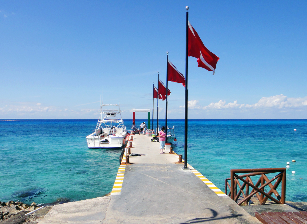 Red flags lined up on a dock with a charter boat waiting in the turquoise water.