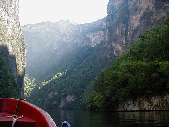 The prow of a boat is visible in a water-level shot of the dramatic sumidero canyon.