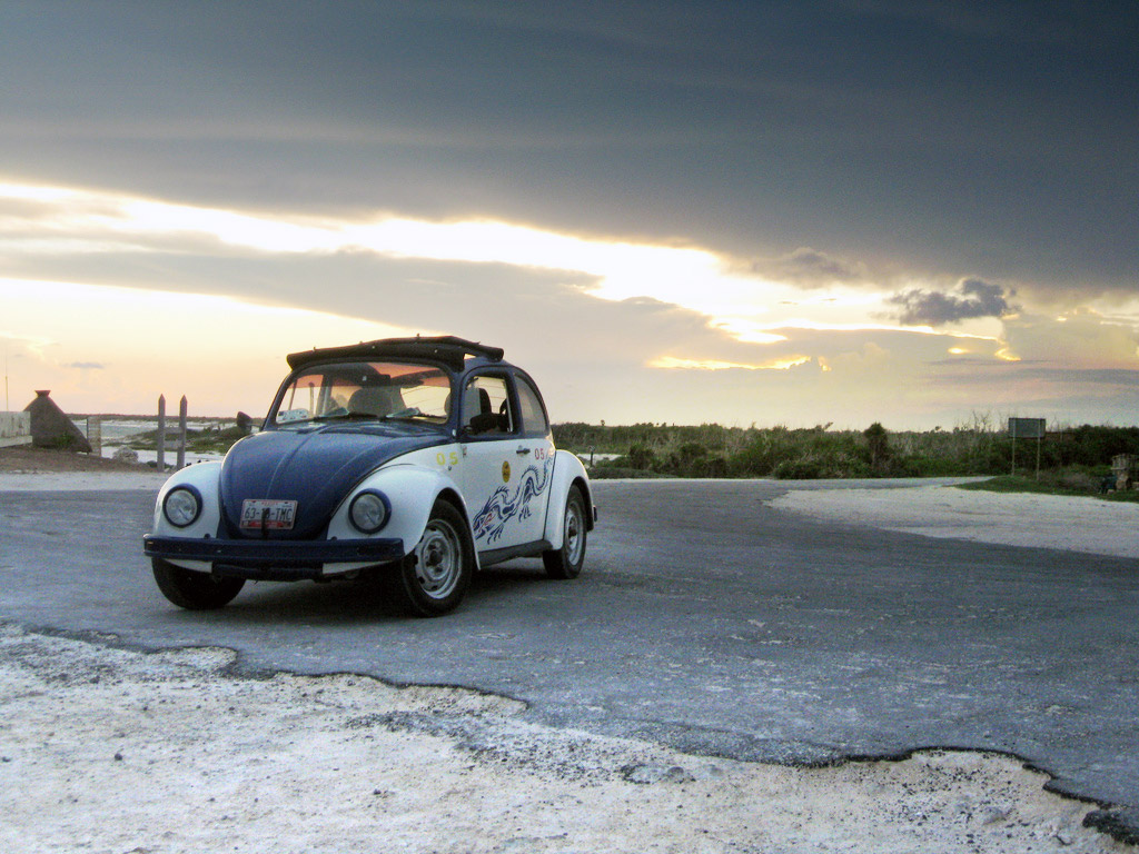 A two-tone volkswagen beetle parked by the beach.