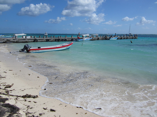 A wooden dock in Puerto Morelos stretches into the water from a white beach dotted with clumps of sea grasses.