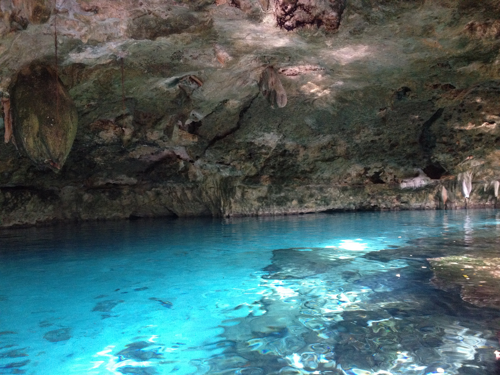 Light reflects off a shallow pool of turquoise water onto the limestone walls above it.