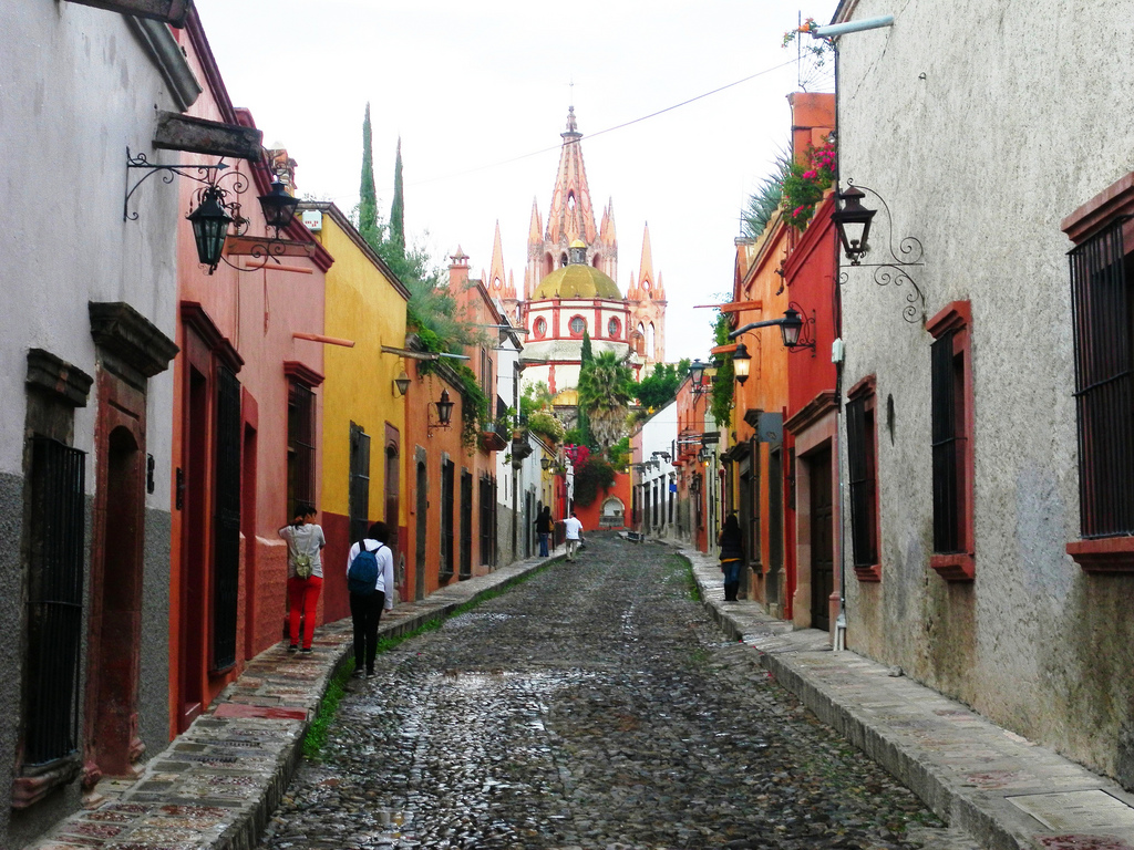View down a cobblestoned streets in San Miguel de Allende with cathedral spires visible in the distance.