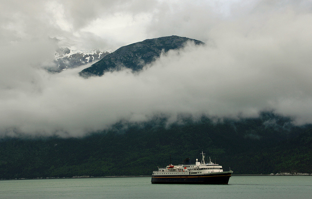 Low, thick clouds obscure the mountains as a ferry crosses the flat water of the inlet.