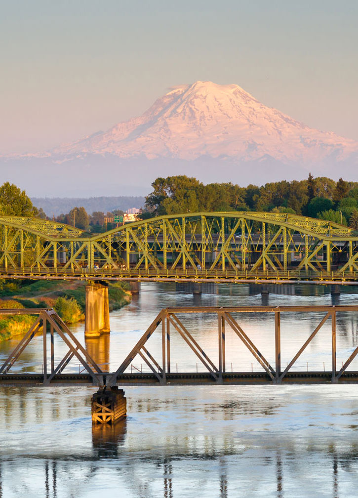 A bridge crosses the Puyallup river with Mount Rainier visible in the distance.