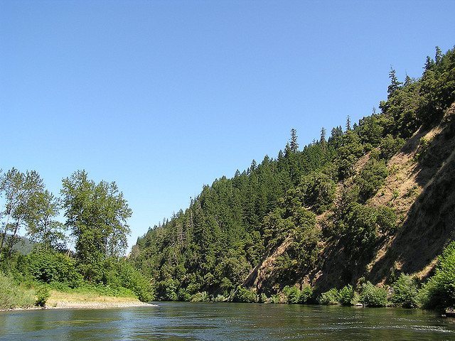 Traveling along a seemingly calm river with a steep hill on one side and a narrow pebbled shore on the other.