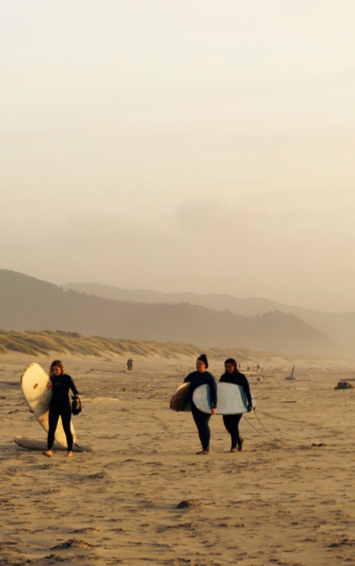 A trio of surfers carrying longboards cross the sand.