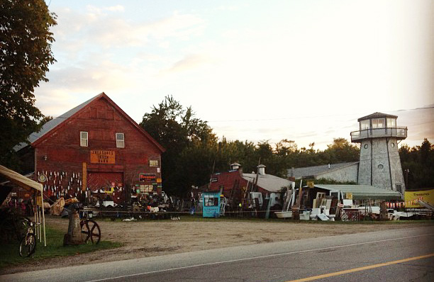 A classic red barn and smaller buildings are stacked with antiques and items for sale.