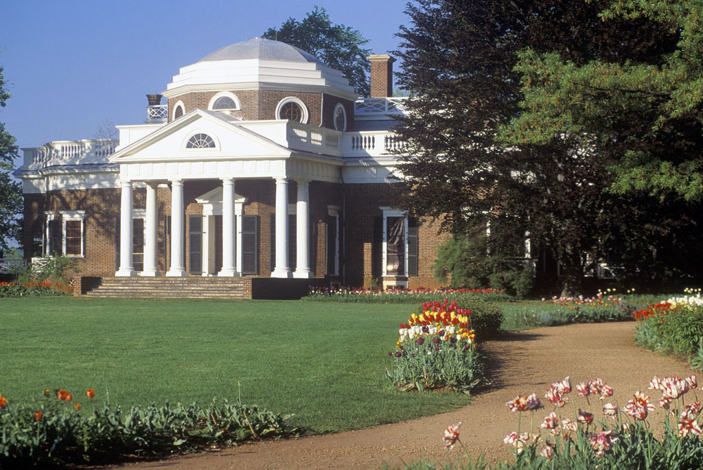 View of the columns of Monticello with a neatly groomed path lined by blooming flowers.