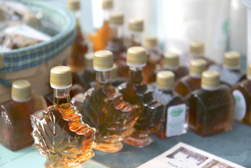 Small bottles of maple syrup shaped like leaves are for sale at a farmers market table.