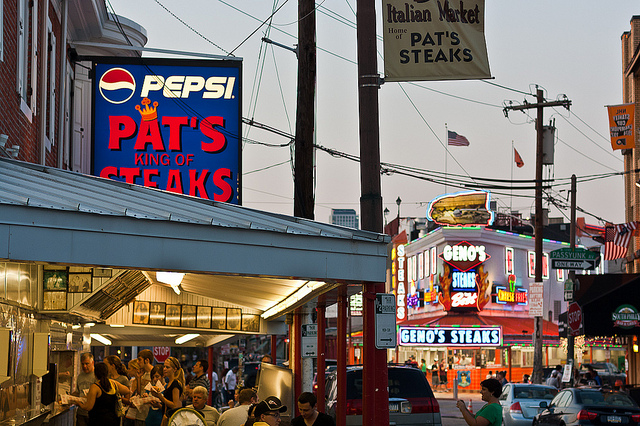 Streetview of the two duelling cheesesteak shops with both of their neon signs visible.