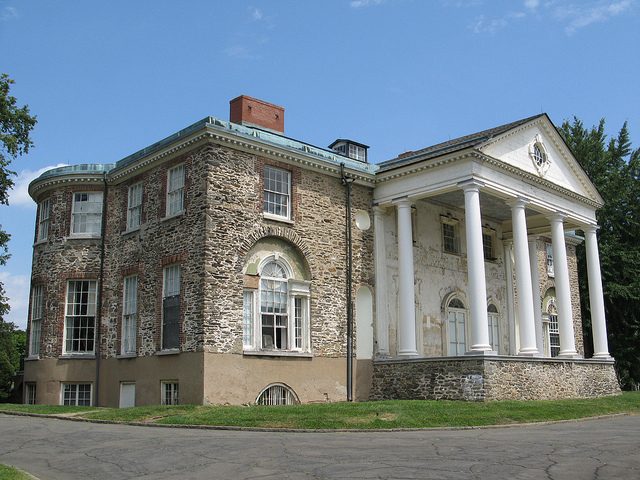 Angled view of a neoclassical mansion with arched windows and columns along the front wall.
