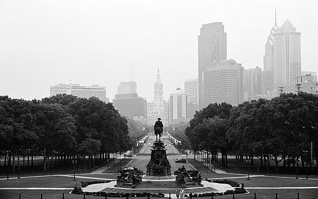 Black and white photo of the skyline receding in the fog behind the stark silhouette of the Ben Franklin statue.