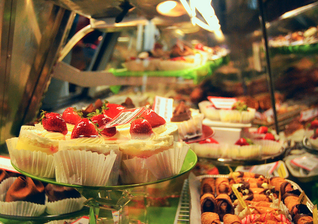 Pieces of strawberry shortcake on a pedestal inside a display case filled with pastries.
