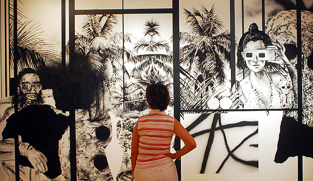 A woman standing contemplating a mural-sized black and white ink-style drawing.