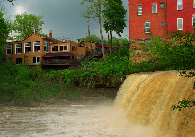 View of a short waterfall with quaint multistory buildings on the bank.