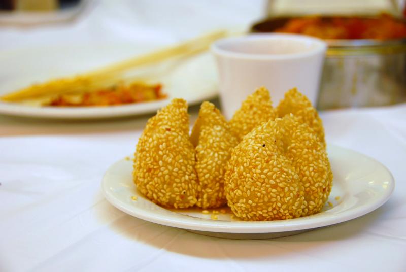 Focus on Sesame Balls on a white plate; doughy drops covered in sesame and fried to golden.