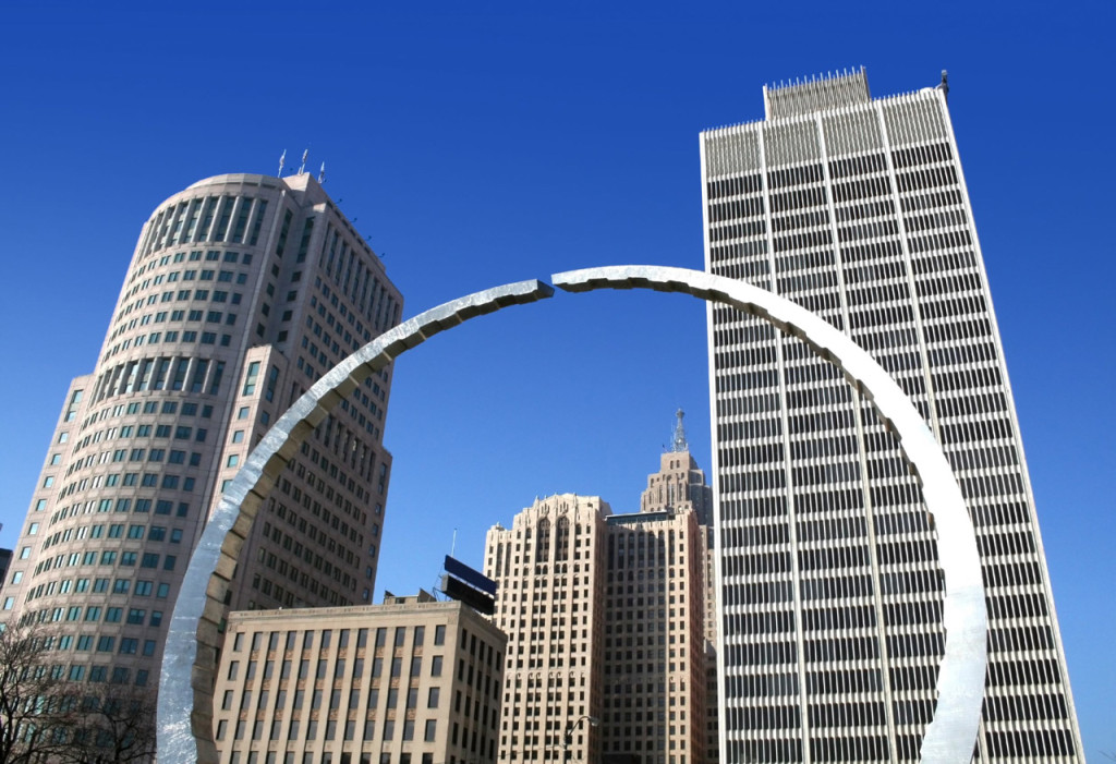 Looking up at a nearly round arch steel sculpture and skyscrapers in downtown Detroit on a perfectly clear day.