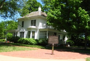 A simple two store whitewashed home surrounded by leafy green trees.