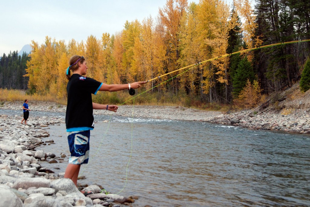 At the edge of a stream, a woman casts a line into the water.