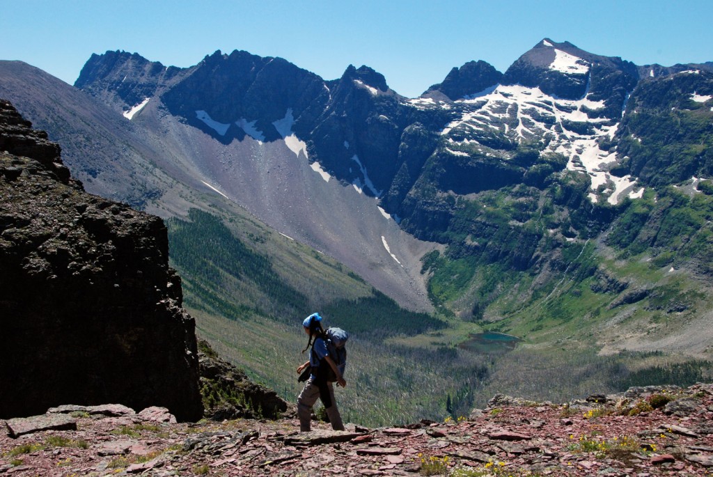 A hiker crosses loose shale stone with an impressive valley vista beyond.