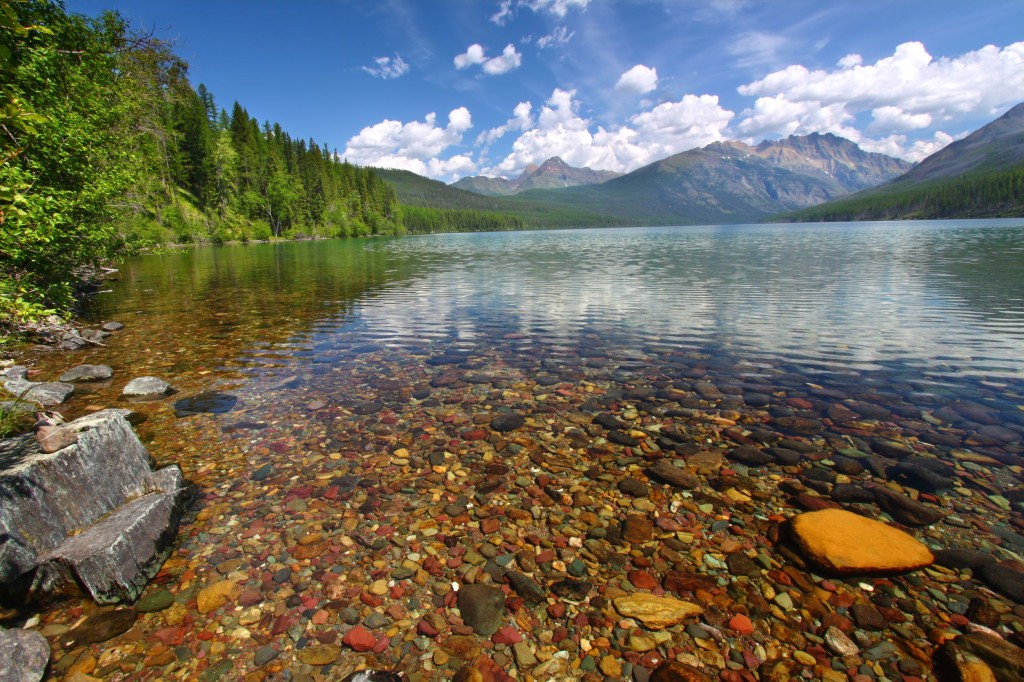 Smooth stones are visible at the clear edge of lake with mountains rising in the distance.