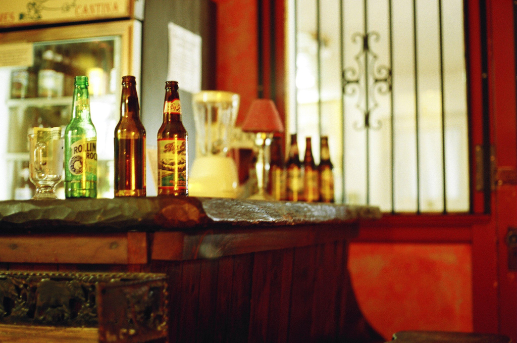 Beer bottles cluster on a heavy, rough-hewn wooden bar top.