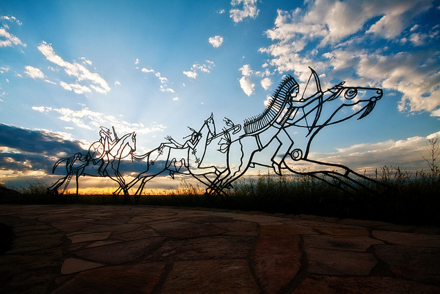 Silhouette of a wireframed sculpture of native american men on horseback.