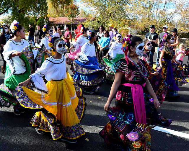 Girls in traditional dress with skull facepaint walk down in the street in the Marigold Parade.