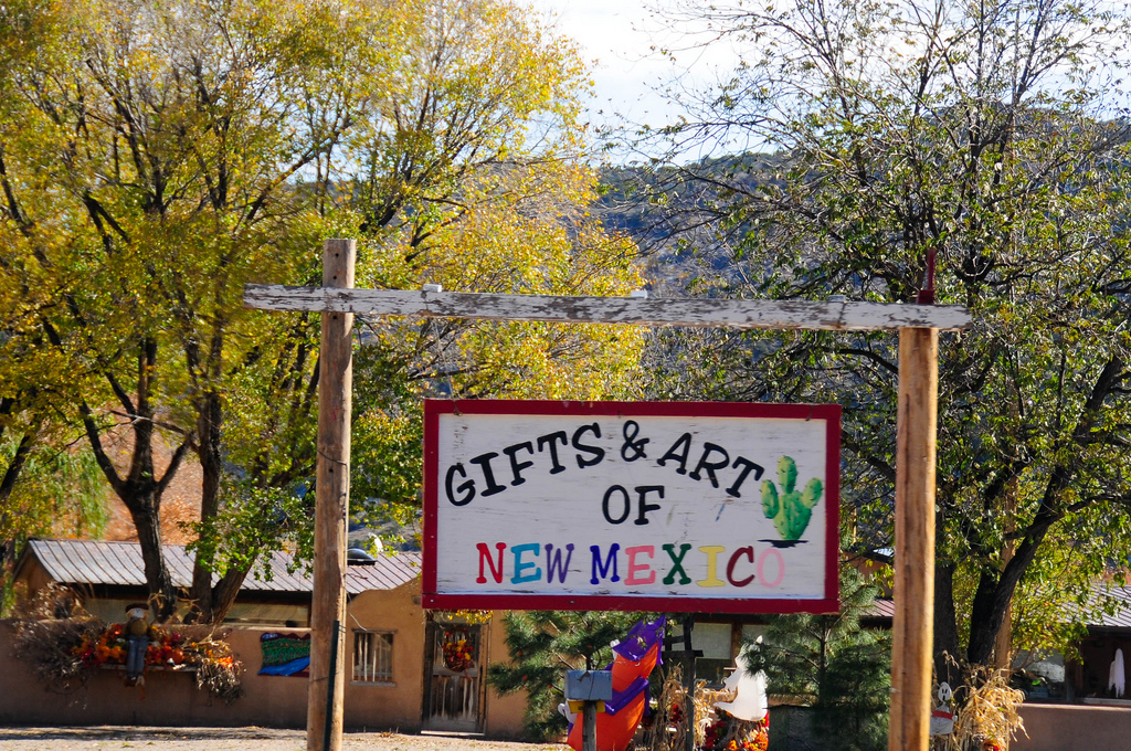 Outside pueblo style buildings a hand-painted wooden sign reads Gifts & Art of New Mexico.