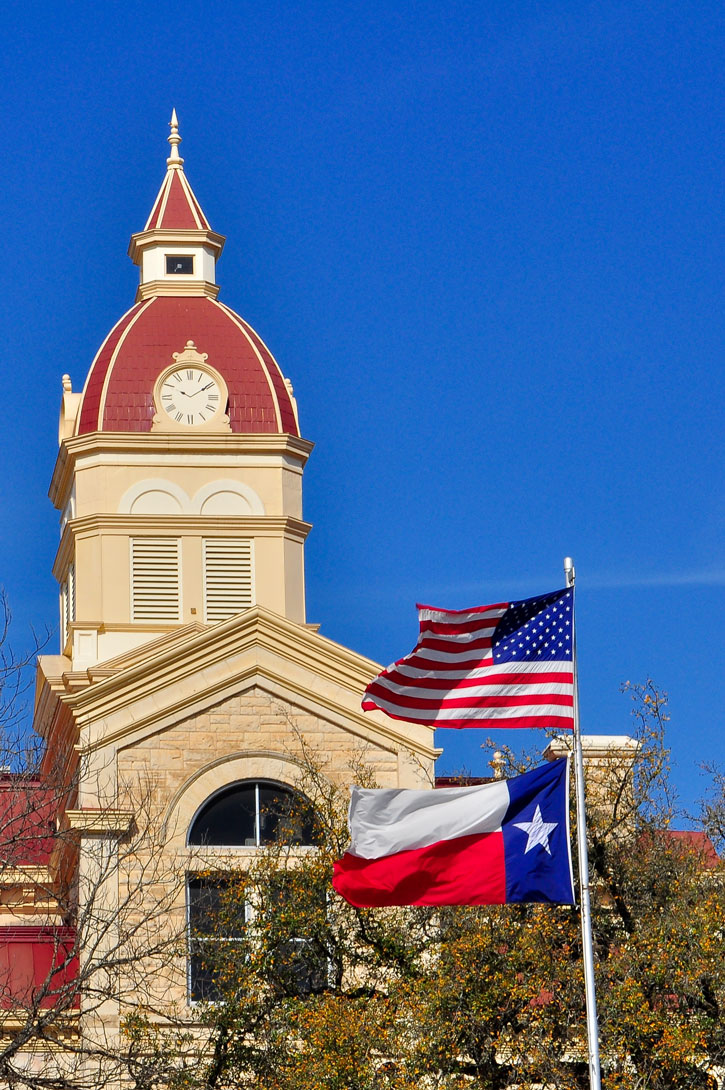 The American and Texas State Flag fly outside the Bandera Courthouse clocktower.