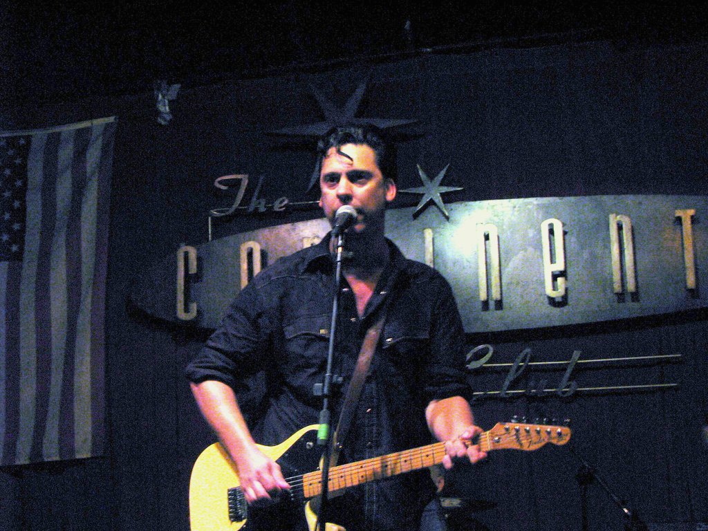 Jesse Dayton singing on stage with an electric guitar and the continental club sign behind him.
