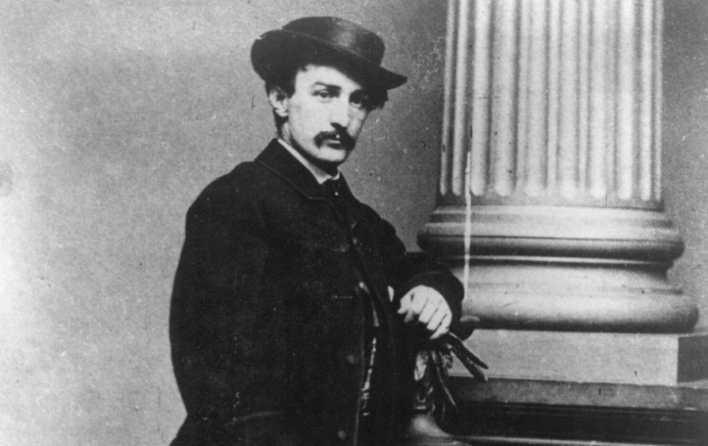 Black and white portrait of John Wilkes Booth standing next to a pillar.