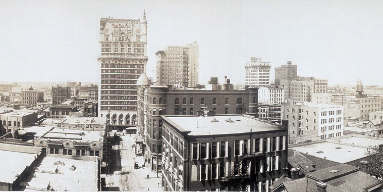 Portion of a panoramic photo with wide streets and the ornamental Hotel Adolphus towering many stories above the nearby buildings.