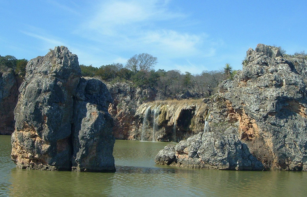 Craggy rocks rise up from the calm surface of a lake while a small waterfall spills down into the lake.