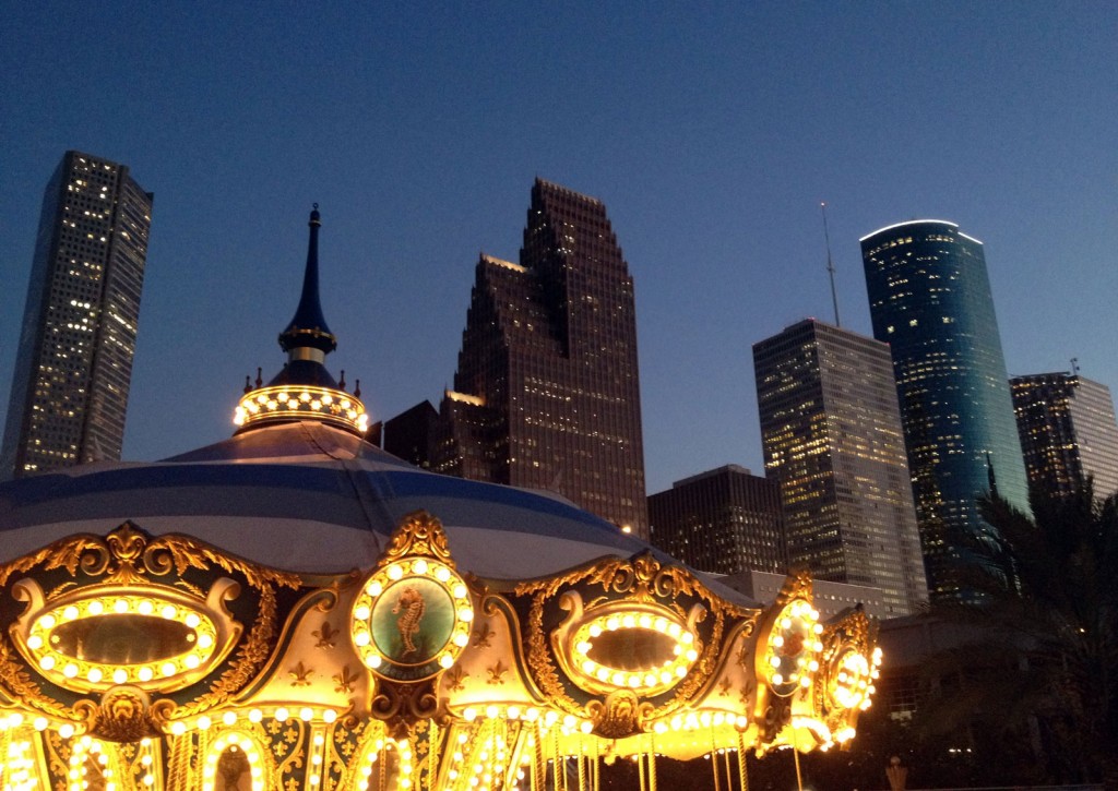 A carousel lights up the foreground while Houston's skyscrapers mark a silhouette against the night sky.
