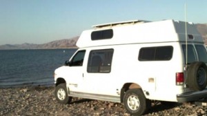 A van converted into an RV is parked lakeside.