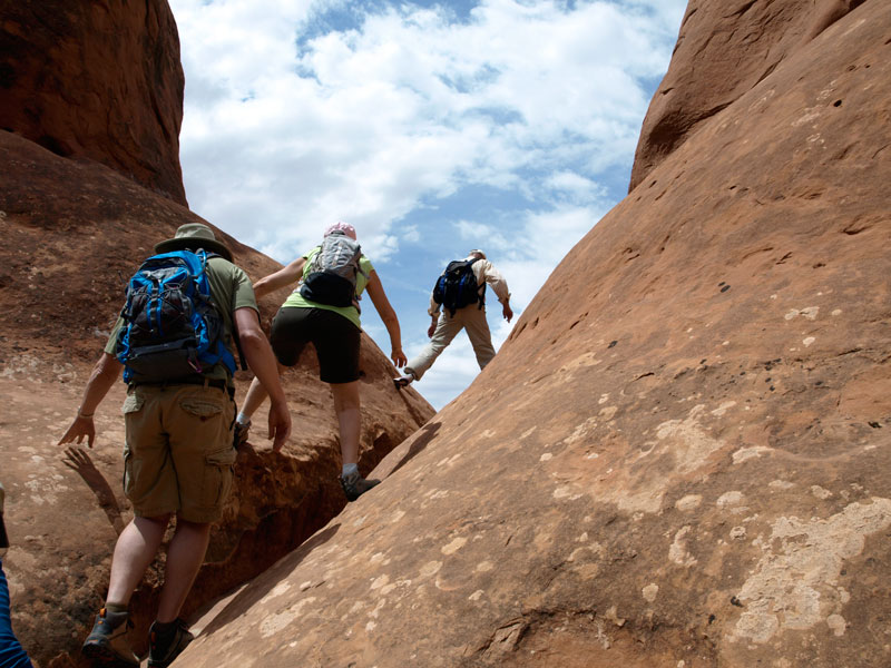 Hikers climb up stone in Arches National Park.