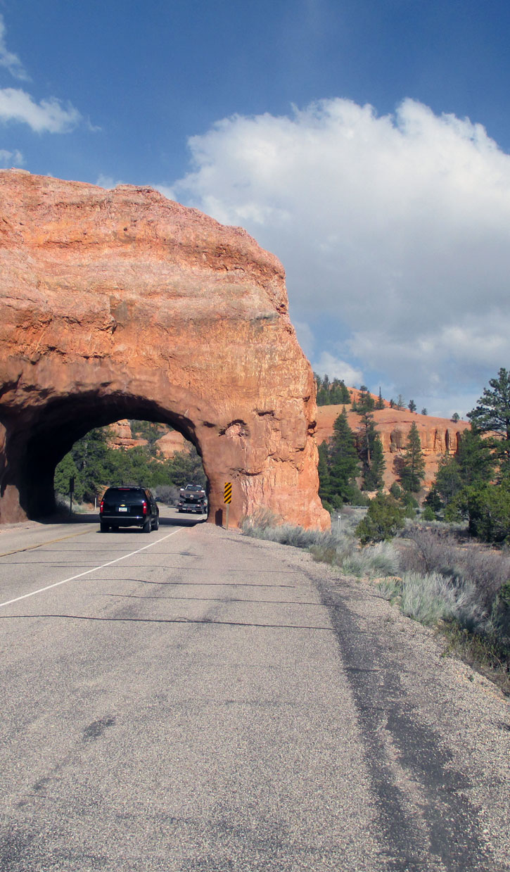 A car on the road passes under a rock arch in Bryce.