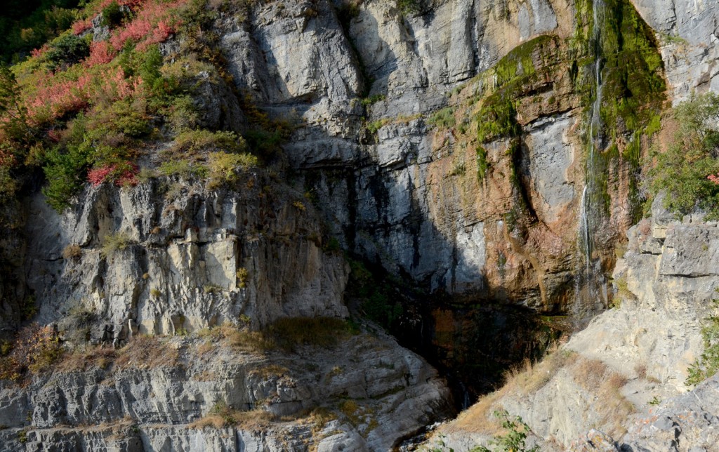 A long waterfall spills down a dramatic rock face with moss and vegetation growing beside the stream.