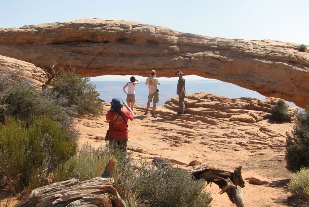 Hikers enjoy and photograph the scenery near a large, low stone arch.