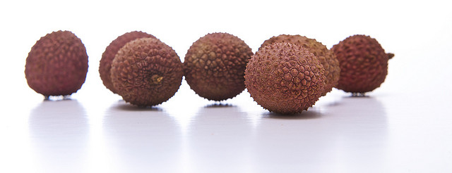 A handful of lychee with reddish pebbled skin on a white glossy surface.