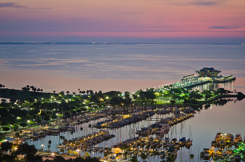 Pastel colors fill the sky over a harbor lit with lights.