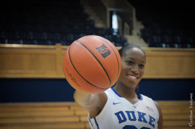 Player Amber Henson in uniform on the court holds the ball out in one hand towards the camera.