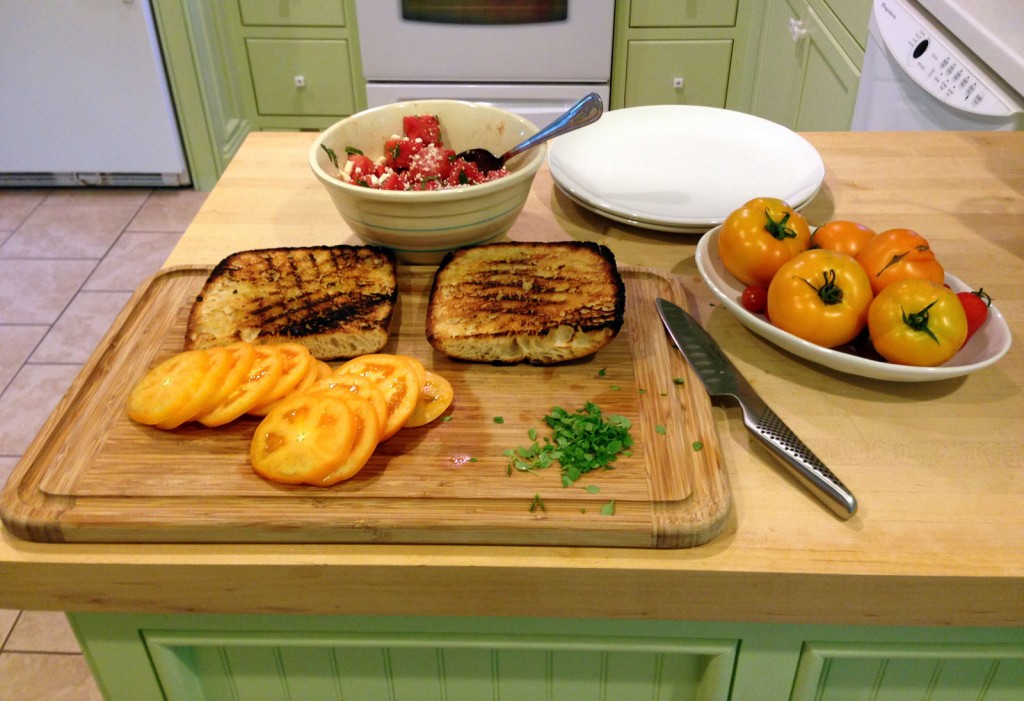 A cutting board with toasted ciabatta and a sliced yellow tomato.