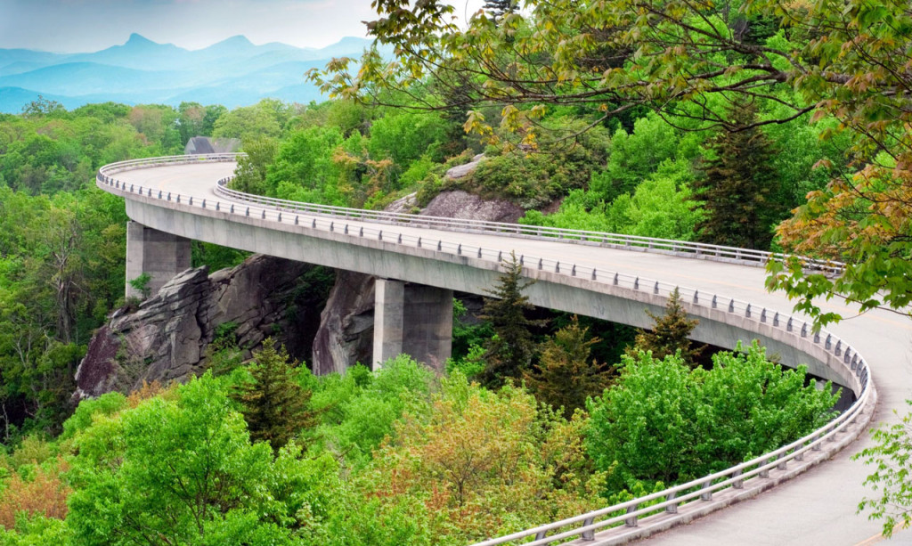 A winding road cuts around the edge of a heavily forested mountain.