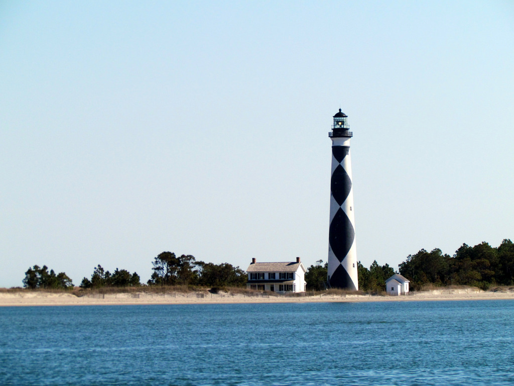 View across the water to a tall lighthouse painted with a black and white harlequin pattern.