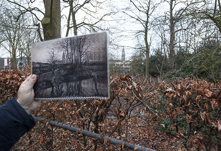 A man holding up a print of one of Van Gogh paintings of Nuenen to compare it with the town today